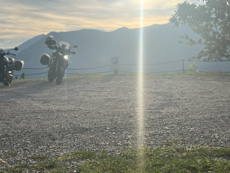 Zwei abgestellte Motorräder auf einem Schotterplatz über dem Tal, die tief stehende Abendsonne scheint durch.